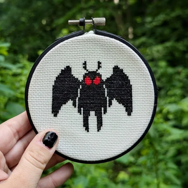 A tiny Mothman hoop held in one hand against a soft green woodland background